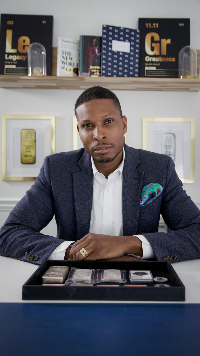 Man in a suit sitting behind a table with a display case, with books and decorative items in the background.
