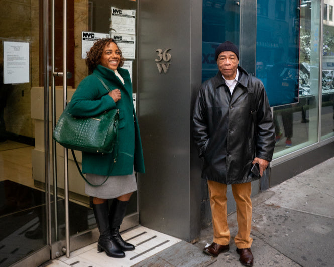 Two people standing outside a building with a glass door and blue wall.