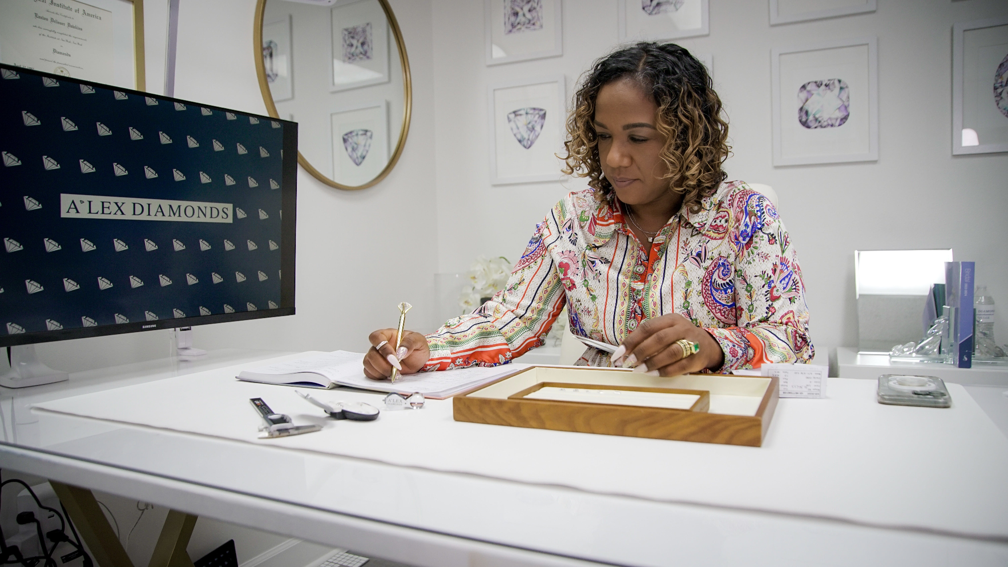 Woman working at a desk with a computer and jewelry display in a diamond store.