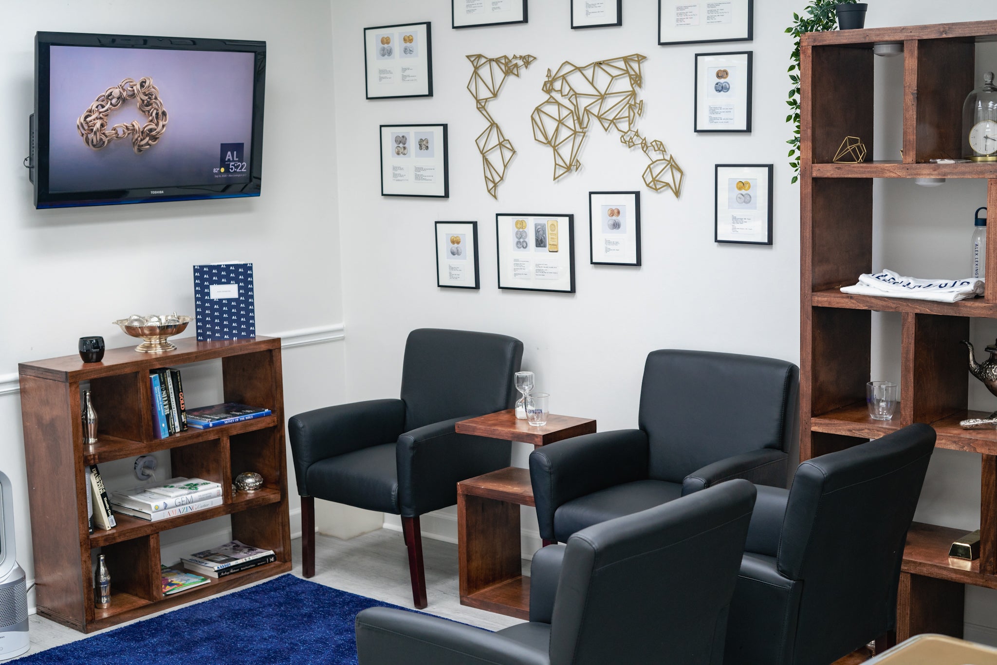 Modern office waiting room with black chairs, wooden bookshelves, and framed pictures on the wall.