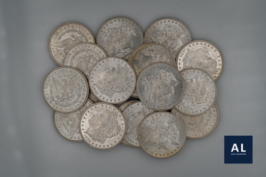 pile of morgan silver dollar coins on a gray background with 'AL' logo.