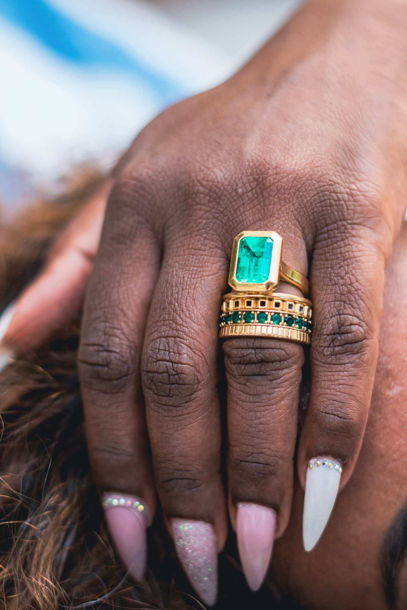 Hand wearing a gold ring with a green gemstone, blurred background